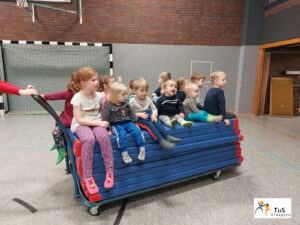 kinderturnen2 Kinder sitzen in der Sporthalle auf dem Mattenwagen