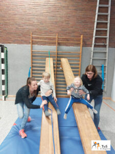 kinderturnen4 Eltern und Kinder rutschen beim Turnen in der Sporthalle auf einer Bank