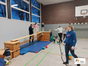 kinderturnen5 Eltern und Kinder gehen beim Turnen in der Sporthalle auf einer Bank