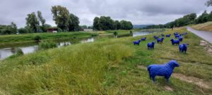 Mehrere Kunstvolle blaue Schafe stehen an einem Fluß auf der Wiese